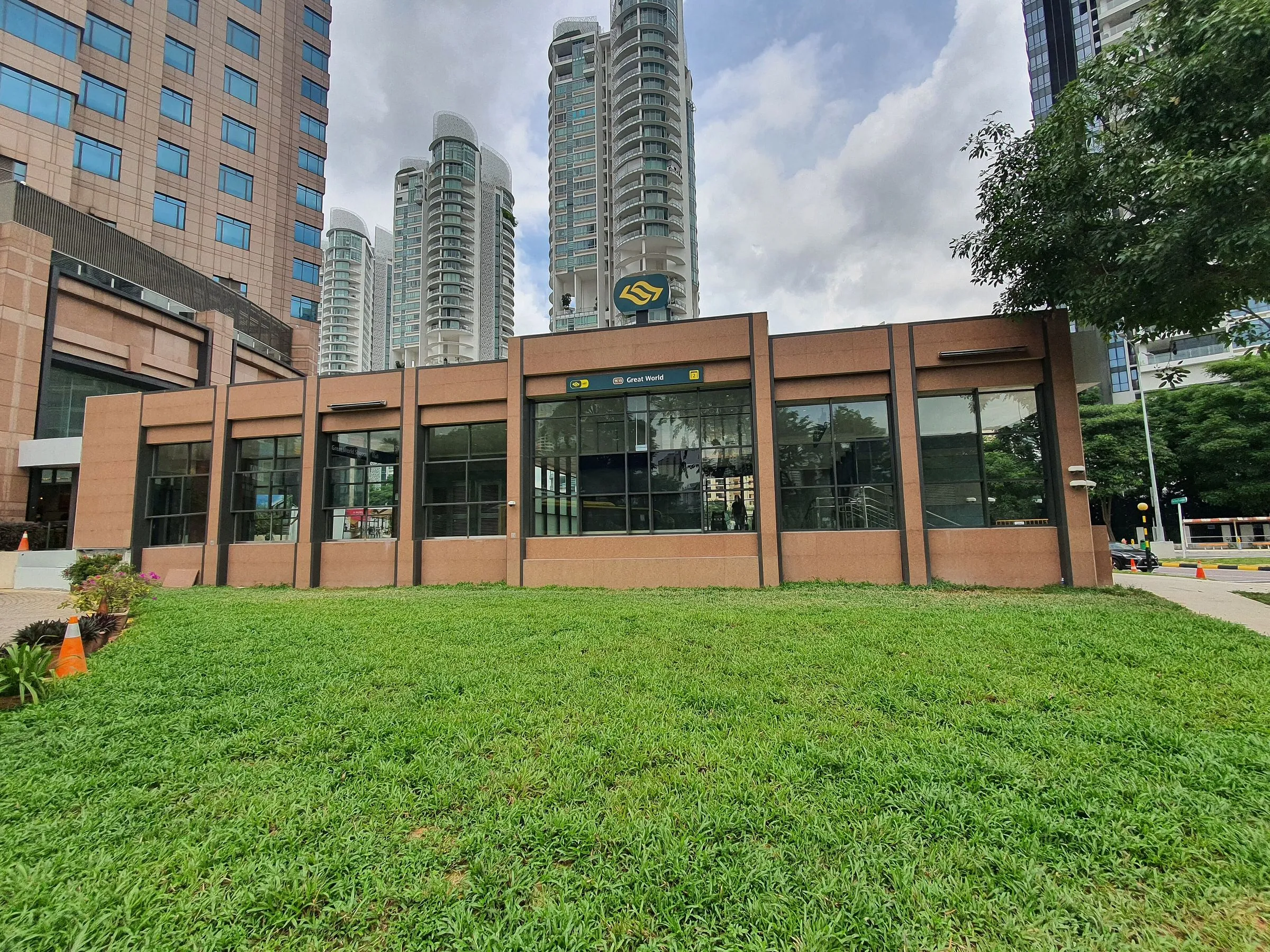 Exit 2 of Great World MRT station, a low single-storey pavilion clad in pink granite with the MRT logo on its roof, behind a lawn and in front of high-rise condominium towers