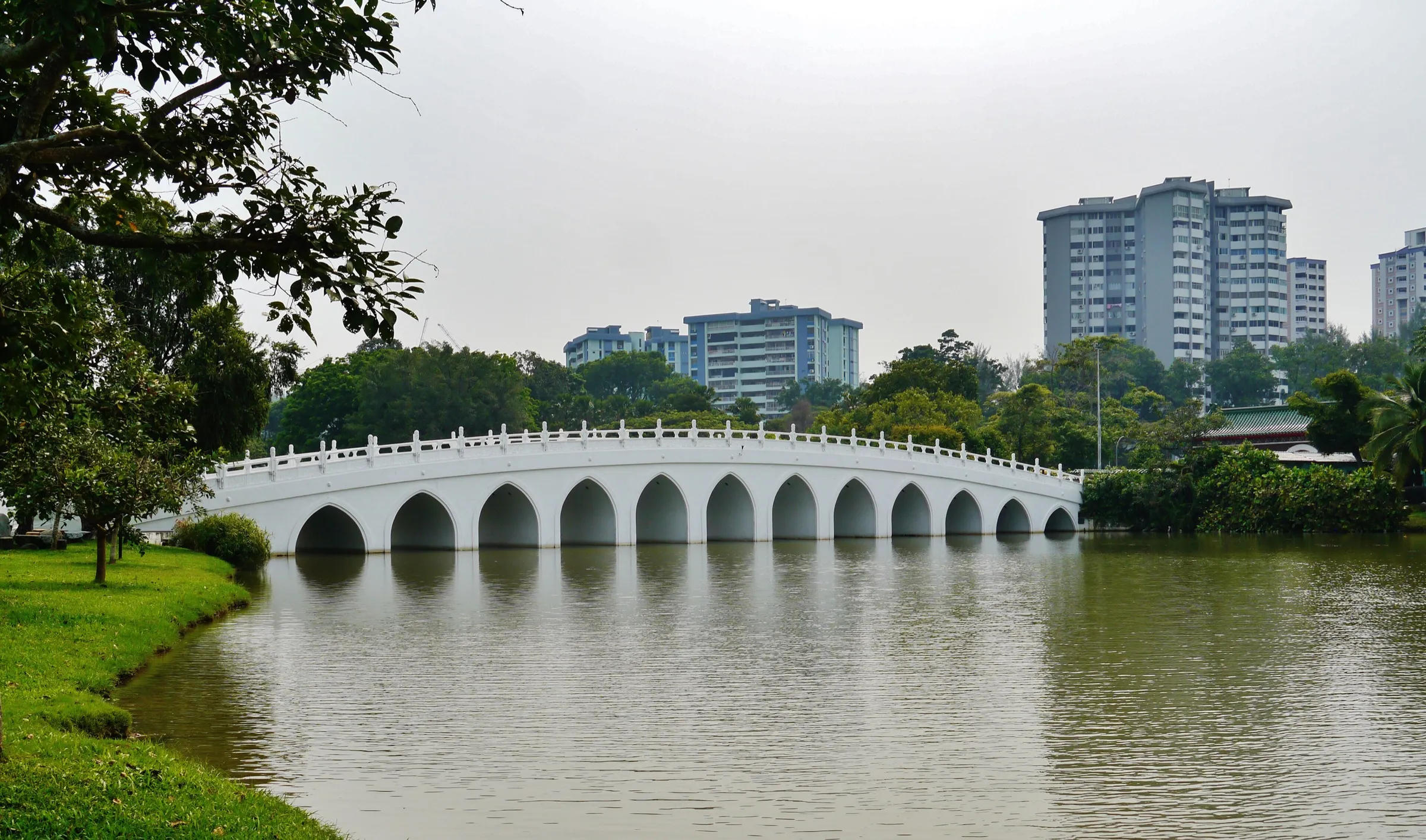 The White Rainbow Bridge, a white multi-arched stone bridge crossing Jurong Lake between the Chinese Garden and Lakeside Garden, with apartment blocks behind the trees