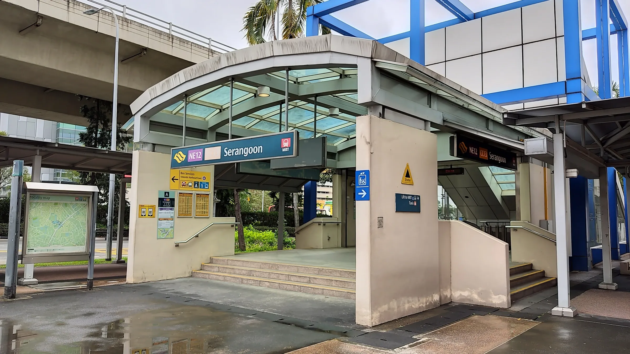 Exit A of Serangoon MRT station, a covered entrance with a curved glass canopy and NE12 CC13 Serangoon signs, beside a blue steel frame structure