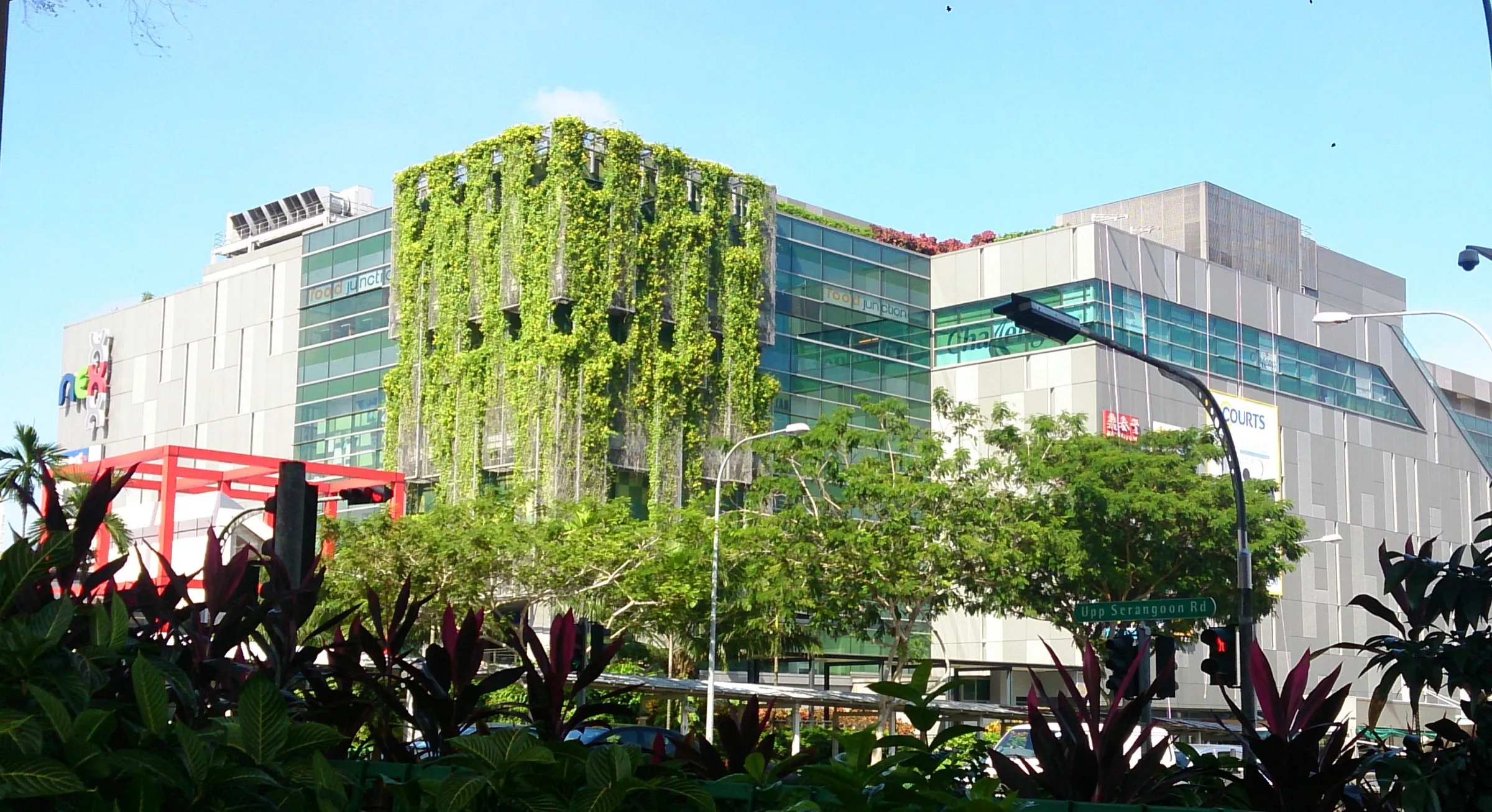 NEX shopping mall at Serangoon Central seen from Upper Serangoon Road, with a green wall of climbing plants on its facade behind roadside trees