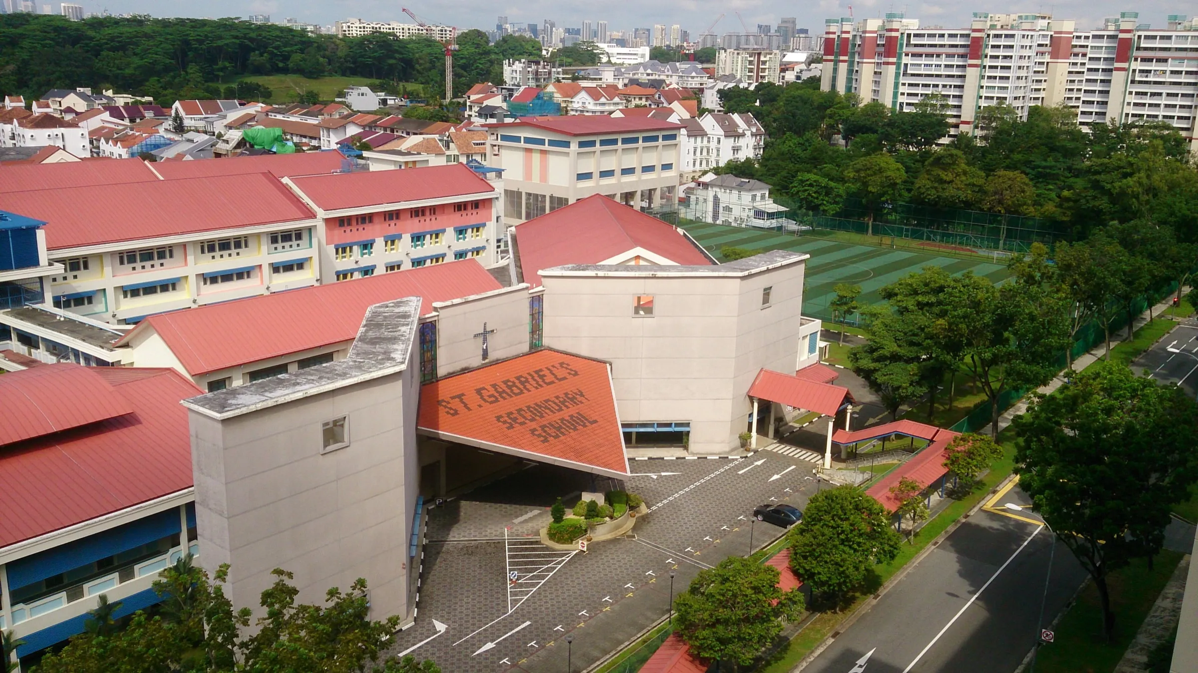 Elevated view of St. Gabriel's Secondary School in Serangoon, with the school name spelt out on an orange tiled roof, red-roofed teaching blocks and a sports field beside the road